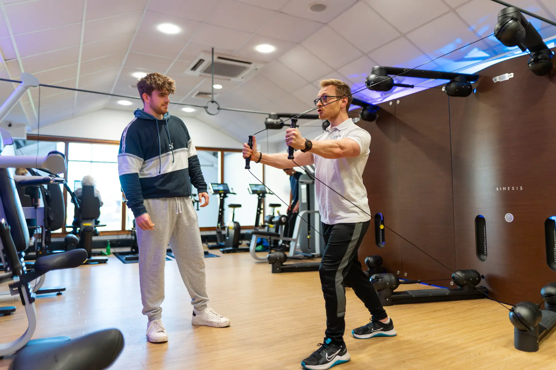 A personal trainer showing a member how to use a Kinesis resistance machine