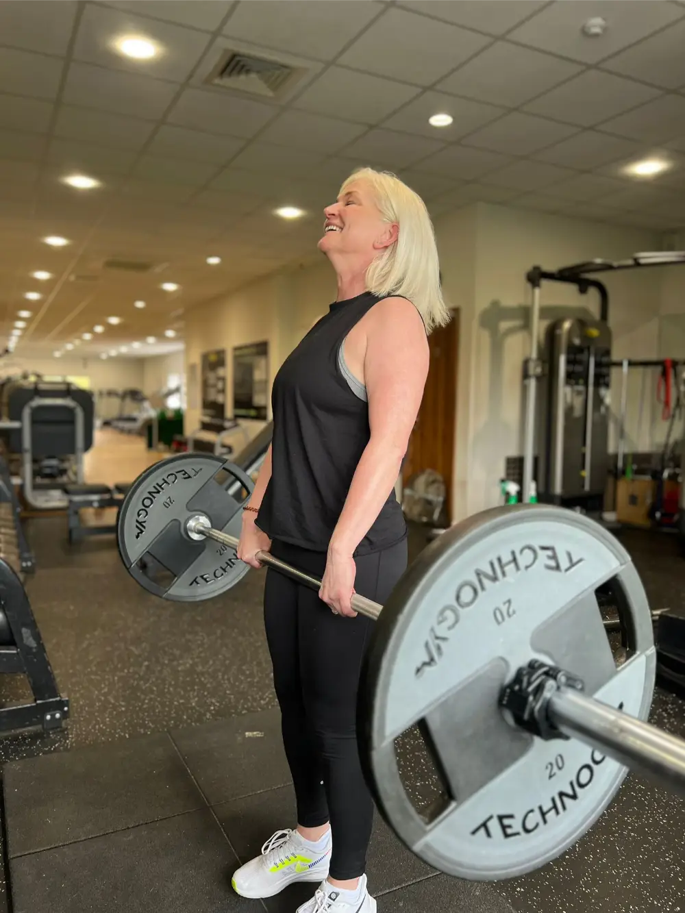 Person standing next to a barbell with weight plates in a gym environment